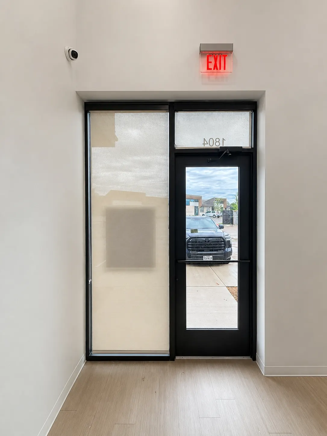Vertical white blinds installed against a black-framed glass entry door in a commercial vestibule.