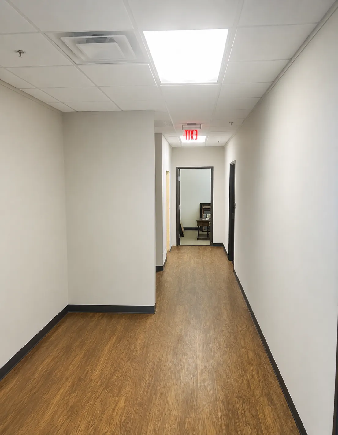 Long office hallway with freshly painted white walls, black trim and wood-look flooring.