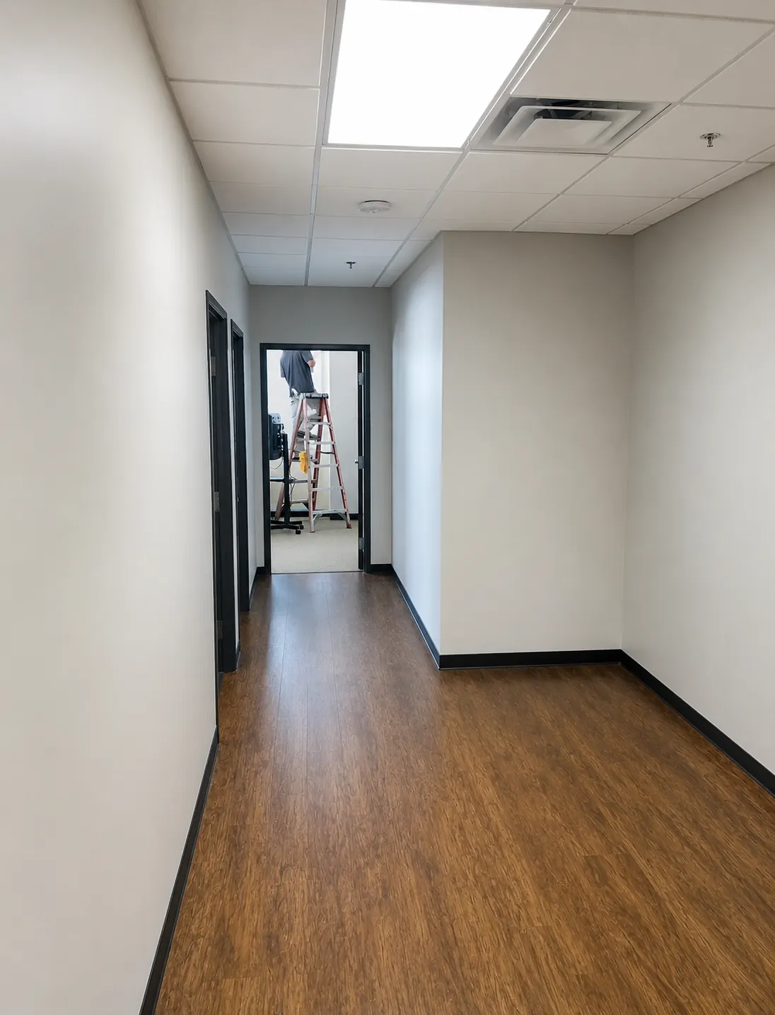 Office hallway being painted, ladder visible at the far end, walls freshly coated.