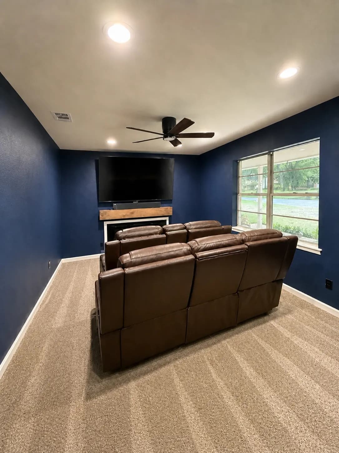 Media room with a wall-mounted TV on a deep-navy accent wall, recliners and a ceiling fan installed.