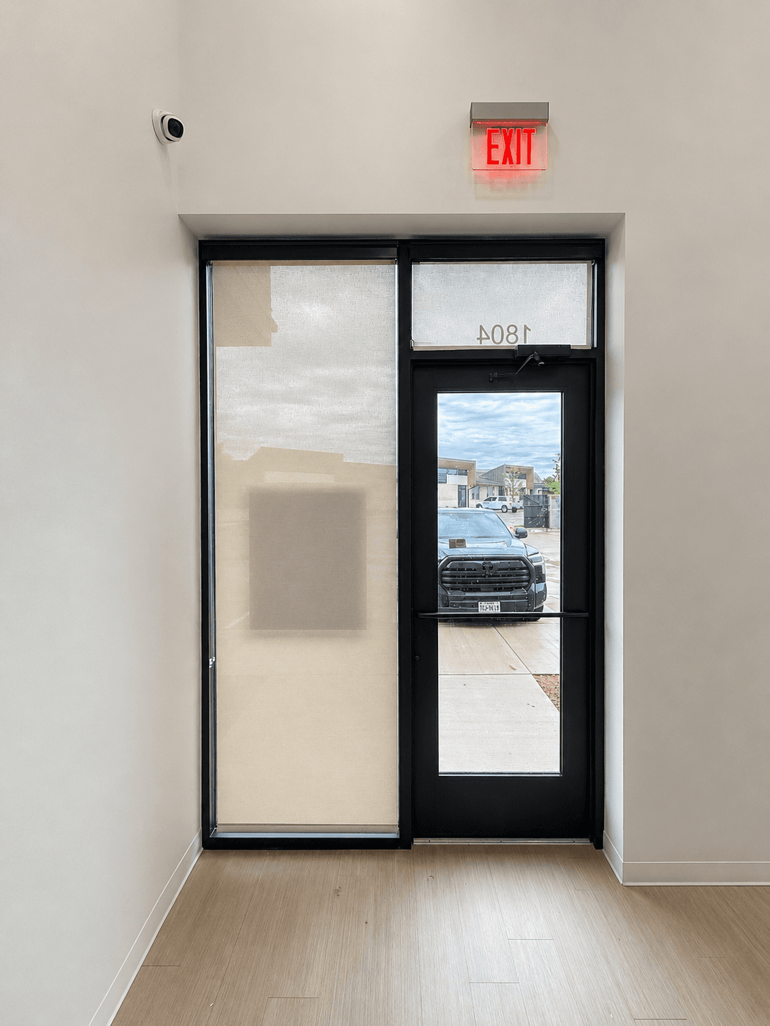 Vertical white blinds installed against a black-framed glass entry door in a commercial vestibule.