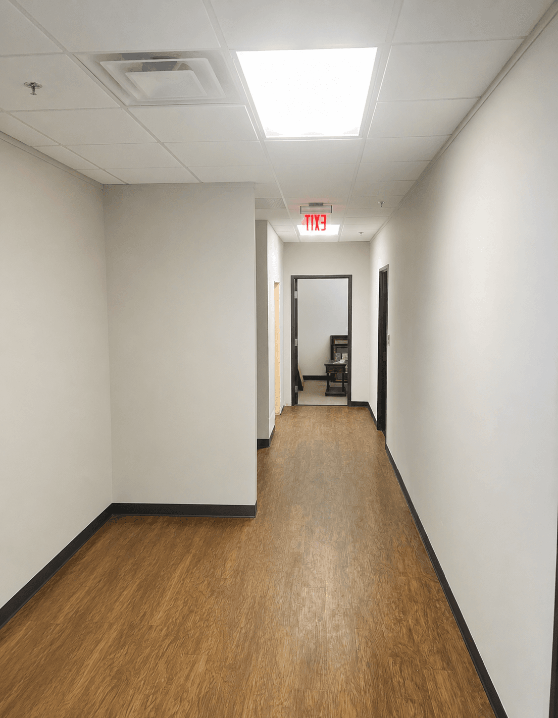 Long office hallway with freshly painted white walls, black trim and wood-look flooring.