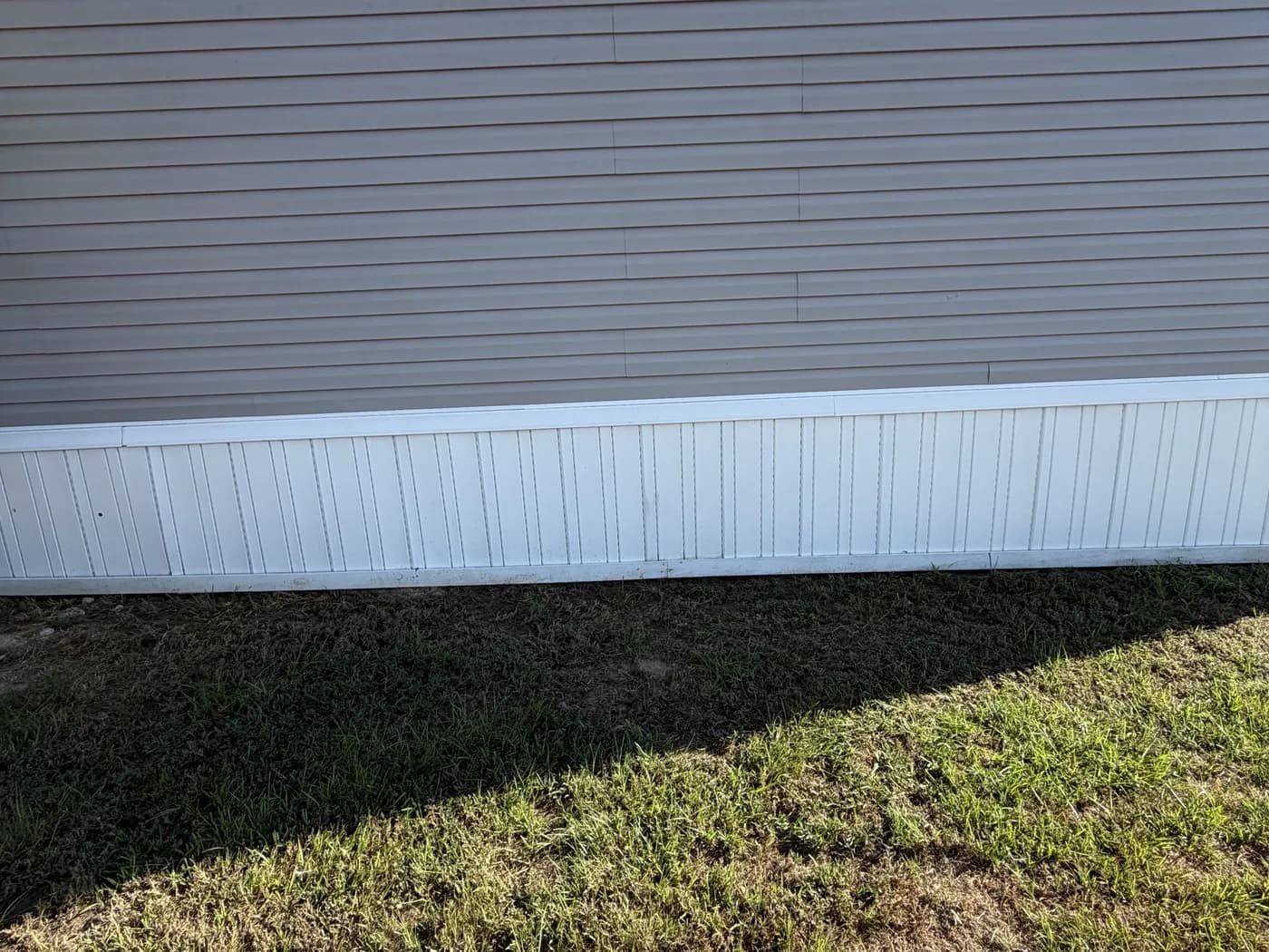 White vinyl skirting running unbroken along the base of a manufactured home under gray lap siding.